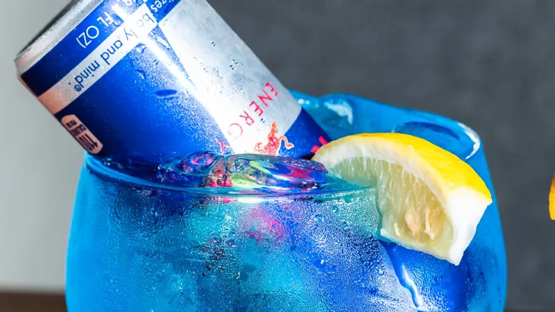Trash Can cocktail — electric blue house drink in a stemmed balloon glass with an upside-down Red Bull can and a lemon wedge
