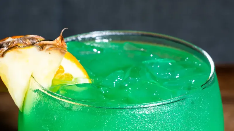 Liquid Marijuana cocktail — vivid green drink in a stemmed glass garnished with pineapple and orange