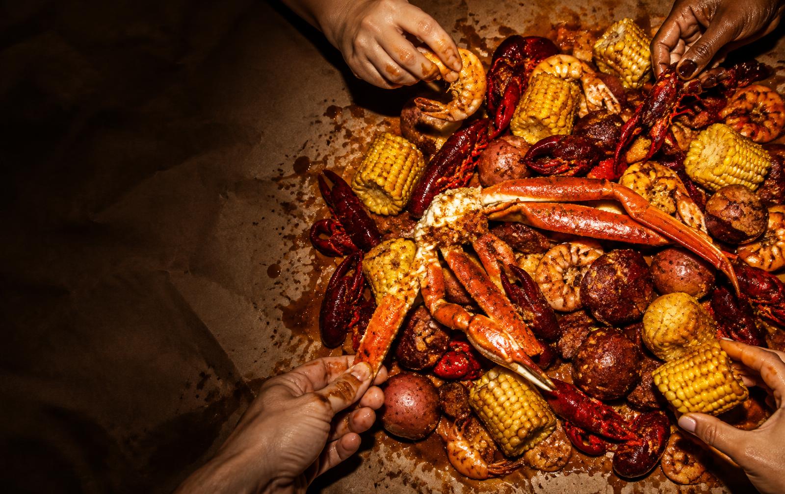 Friends reaching into a shared Cajun seafood boil at Big Crab in Jacksonville, FL